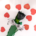 Black rose with a white ribbon on a white background with red heart shapes and text.