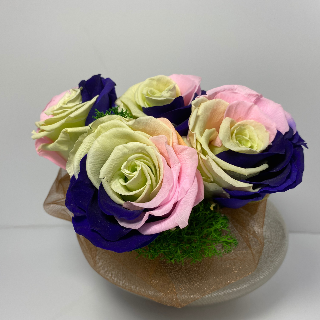 Side profile. 4 extra large prile preserved roses (light green, dark purple, pink mixture) nestled on green preserved moss displayed on pearl shaped copper glass vase 