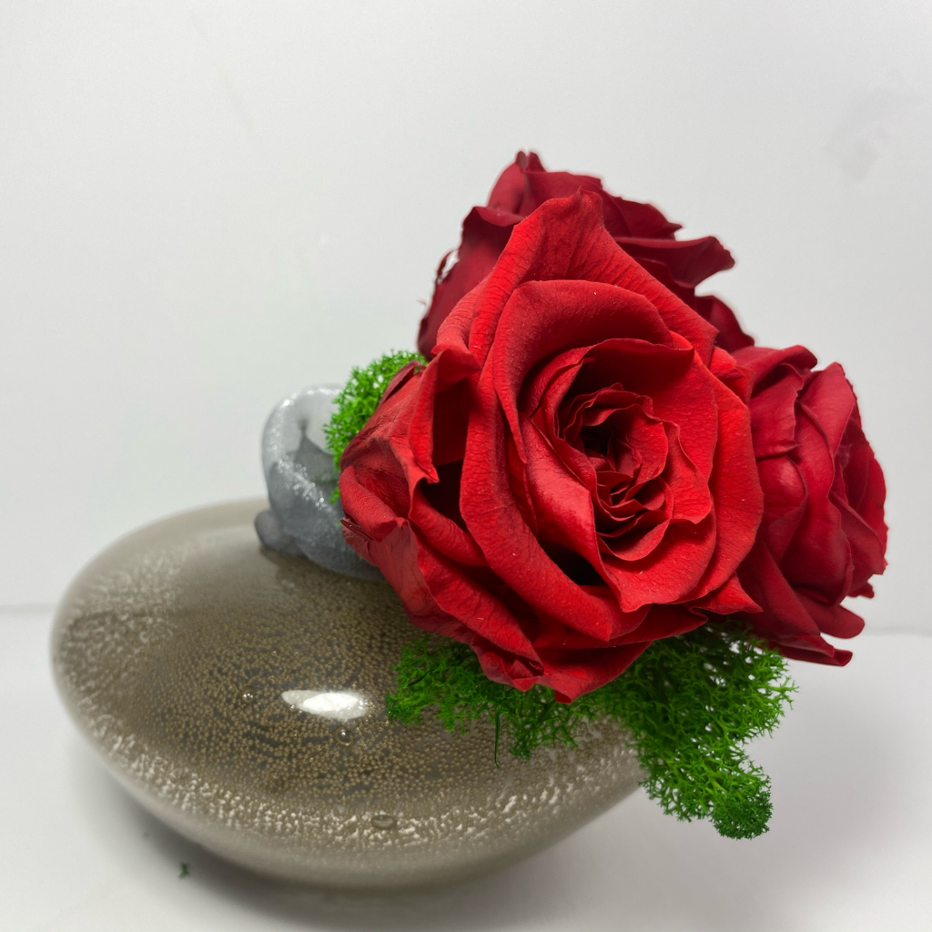 Side Profile. 4 extra large red preserved roses nestled on green preserved moss displayed on pearl-shape copper glass vase 