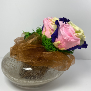 Side profile. 4 extra large prile preserved roses (light green, dark purple, pink mixture) nestled on green preserved moss displayed on pearl shaped copper glass vase 